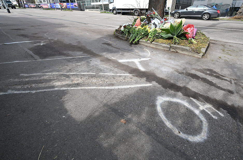 Blumen liegen an einer Unfallstelle nach einem mutmaßlichen Autorennen mit zwei Toten. Davor sind Kreidezeichen und Unfallspuren auf dem Pflaster.