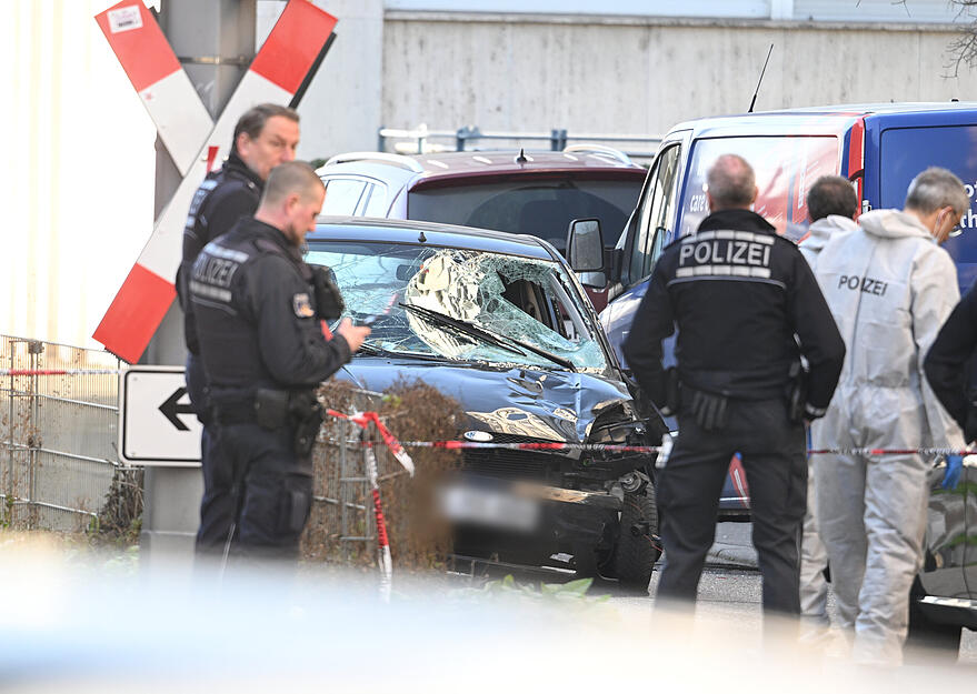 Einsatzkräfte der Polizei stehen bei einem Großeinsatz neben einem beschädigten Fahrzeug in der Innenstadt.