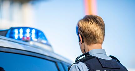 Eine Polizistin steht vor einem Streifenwagen.