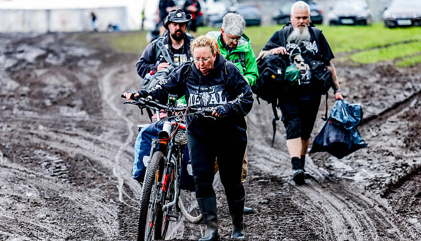 Festivalbesucher verlassen das verschlammte Campinggel&auml;nde des Wacken Open Air mit ihren Fahrr&auml;dern. Foto: Axel Heimken/dpa