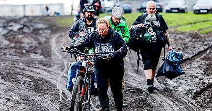 06.08.2023, Schleswig-Holstein, Wacken: Festivalbesucher verlassen das verschlammte Campinggelände des Wacken Open Air mit ihren Fahrrädern. Foto: Axel Heimken/dpa +++ dpa-Bildfunk +++