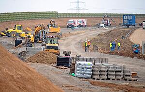 80 Prozent des Baustellenverkehrs flie&szlig;t &uuml;ber eine neu angelegte Stra&szlig;e. Sie wird sp&auml;ter zur Kreisstra&szlig;e ausgebaut. Ein L&auml;rmschutzwall (gr&uuml;n) ist bereits fertig.