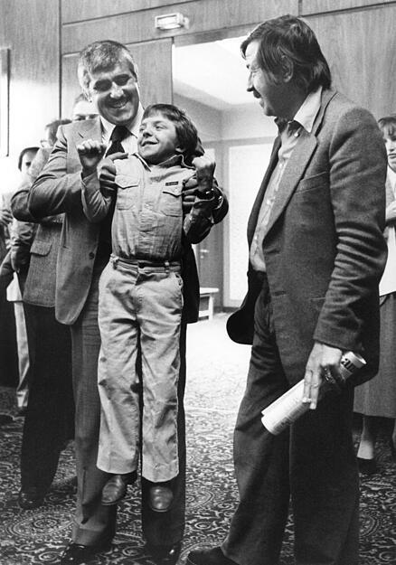 David Bennent, der damals 12-j&auml;hrige Hauptdarsteller von "Die Blechtrommel", wird auf der Pressekonferenz vor der Urauff&uuml;hrung des Films von seinem Filmvater Mario Adorf hochgehoben. Rechts der Autor der Romanvorlage.