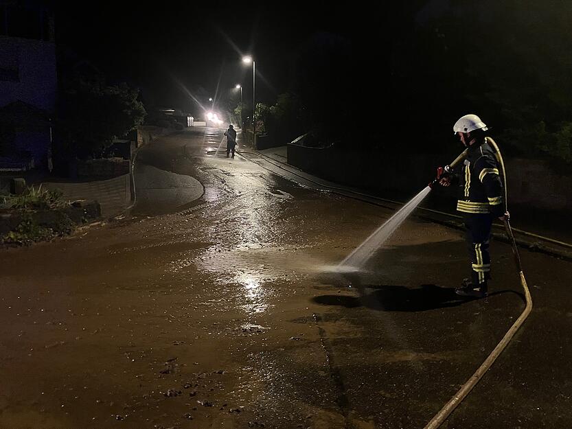 Ein Feuerwehrmann spritzt in einer Straße in Stein den Schlamm beiseite.
