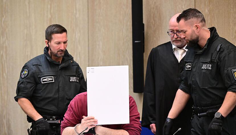 Der Angeklagte in einem Mordprozess nach einer Todesfahrt von Mannheim sitzt mit einem Aktendeckel vor seinem Gesicht im Gerichtssaal, rechts neben ihm steht sein Verteidiger Uwe Kosmala. (Archivbild)