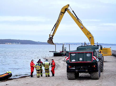 Helfer stehen am Strand in der N&auml;he des gestrandeten Wals.