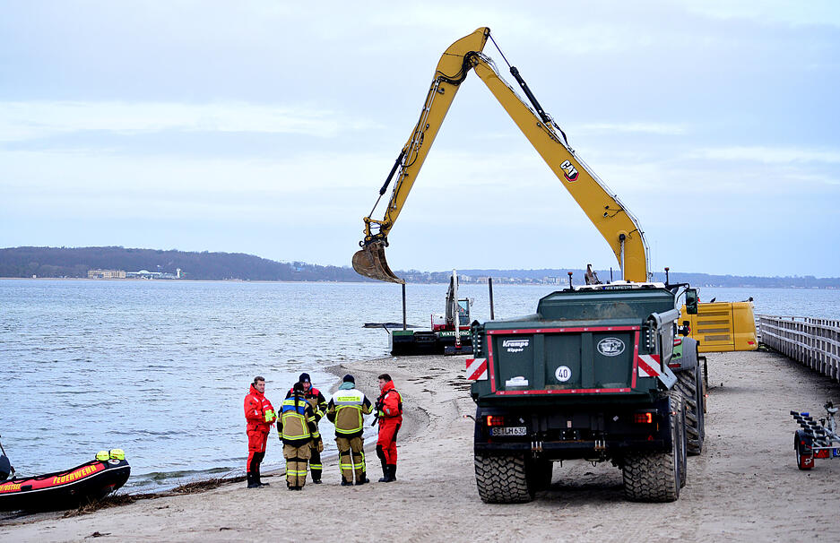 Helfer stehen am Strand in der N&auml;he des gestrandeten Wals.