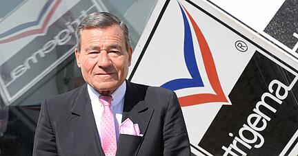 Wolfgang Grupp steht am Firmensitz in Burladingen vor einem Firmenlogo.