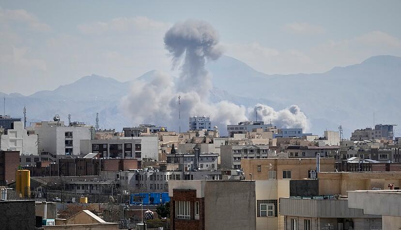 Menschen in Teheran (Iran) beobachten von einem Dach aus, wie eine Rauchwolke nach einer Explosion aufsteigt.