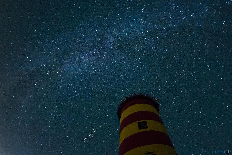 Eine Sternschnuppe leuchtet am 13.08.2015 über dem Pilsumer Leuchtturm in Pilsum (Niedersachsen) am Nachthimmel. Zudem ist oben die Milchstraße zu sehen.
