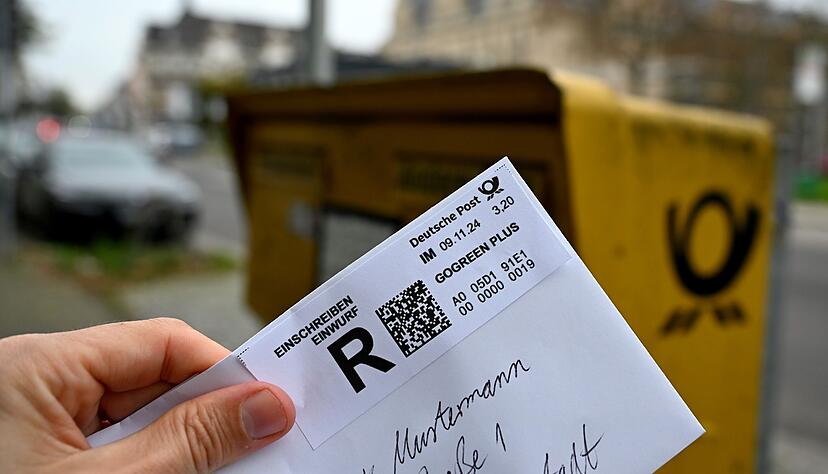 Ein Mann hält ein sogenanntes Einwurf-Einschreiben vor einen Briefkasten (gestellte Szene). Ein Mann hält ein sogenanntes Einwurf-Einschreiben vor einen Briefkasten (gestellte Szene).
