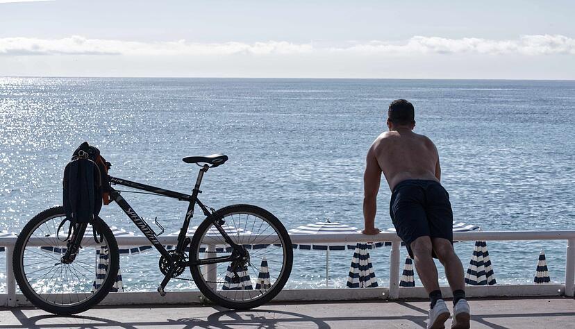 Ein Mann mit nacktem Oberk&ouml;rper macht am Strand von Nizza neben seinem Fahrrad &Uuml;bungen. (Archivbild)