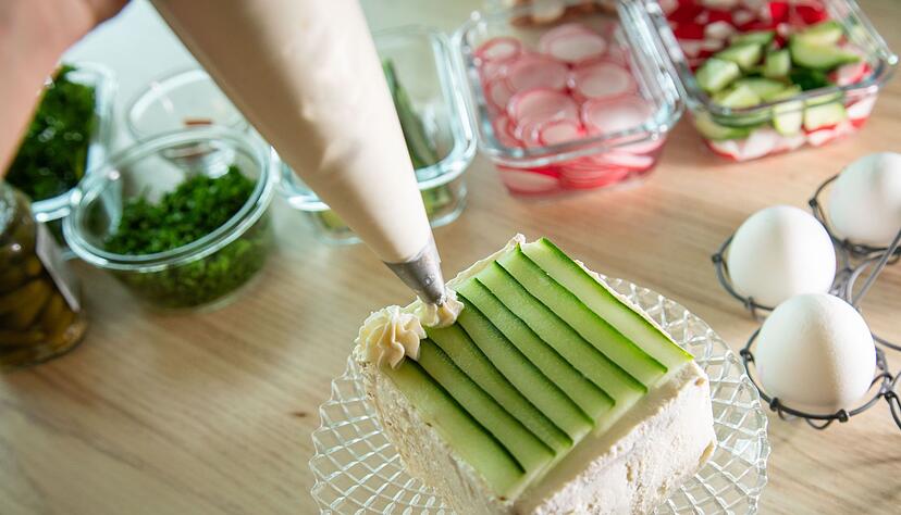 Auf der Gurkenschicht wird mit einem Spritzbeutel Frischkäse in Rosettenform aufgespritzt. Auf der Gurkenschicht wird mit einem Spritzbeutel Frischkäse in Rosettenform aufgespritzt.
