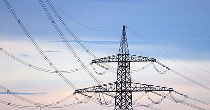 Windr&auml;der stehen hinter dem Mast einer Stromtrasse.