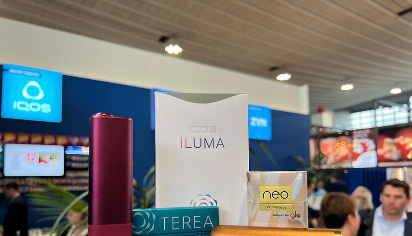 Ein Tabakerhitzer der Marke Iqos vom Hersteller Philip Morris und ein dazugeh&ouml;riges P&auml;ckchen Tabaksticks der Marke Terea sowie das Konkurrenzprodukt Glo (mit Neo-Tabaksticks) des Herstellers BAT liegen bei der Fachmesse Intertabac in einer Messehalle.