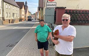 Marcus Rudlof (links) mit Nachbar Reinhard Mader und Hahn Fridolin stehenan der Siegelsbacher Hauptstraße, durch die täglich Schwerlastverkehr rollt. Gleich nebenan hält Rudlof seine Hühner. Marcus Rudlof (links) mit Nachbar Reinhard Mader und Hahn Fridolin stehenan der Siegelsbacher Hauptstraße, durch die täglich Schwerlastverkehr rollt. Gleich nebenan hält Rudlof seine Hühner.