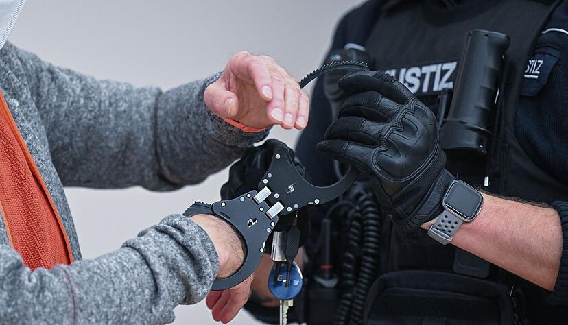 Ein angeklagter, mutmaßlicher Reichsbürger (l) bekommt vor Prozessbeginn die Handschellen abgenommen. Ein angeklagter, mutmaßlicher Reichsbürger (l) bekommt vor Prozessbeginn die Handschellen abgenommen.