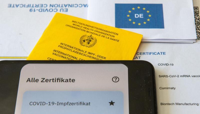 Ein Impfpass und ein Smartphone liegen auf einem Impfzertifikat.