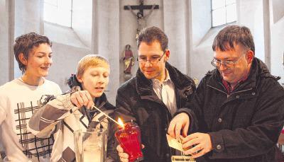 &Ouml;kumenisches Zeichen: Henri Scheppach gibt das Friedenslicht an Ingo Kuhbach weiter. Jonah Schmelzer (links) und Ulrich Hartmann schauen zu.Foto: Ralf Reichert