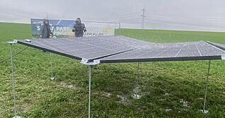 Sarah von Keudell hält mit dem Wasserschlauch auf die PV-Module und simuliert damit einen starken Regenguss. Das Wasser fließt über die Zwischenräume ab.