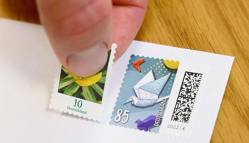 Eine 10-Cent-Briefmarke wird neben eine 85-Cent-Briefmarke geklebt (gestellte Szene). Eine 10-Cent-Briefmarke wird neben eine 85-Cent-Briefmarke geklebt (gestellte Szene).