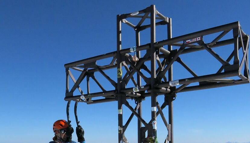Ein Bergsteiger macht an seinen Eisgeräten einen Klimmzug am Gipfelkreuz der Marmolada. Ein Bergsteiger macht an seinen Eisgeräten einen Klimmzug am Gipfelkreuz der Marmolada.