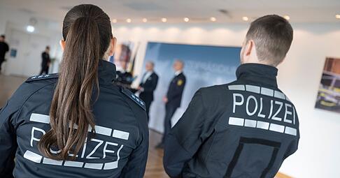 Zwei Polizeibeamten, die neue Uniformen anhaben, verfolgen eine Pressekonferenz.