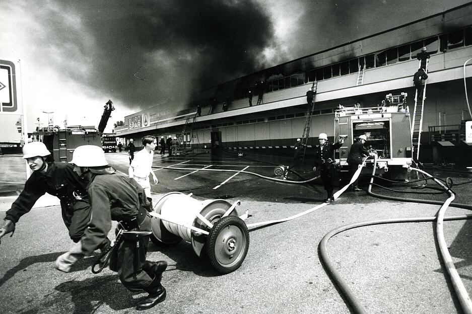 19.06.1985: Die Flammen breiten sich explosionsartig aus und finden im Sortiment von Farben, Lösungsmitteln, Teppichen und Kunststoffen reichlich Nahrung. Die Feuerwehr rückt mit 20 Fahrzeugen an.