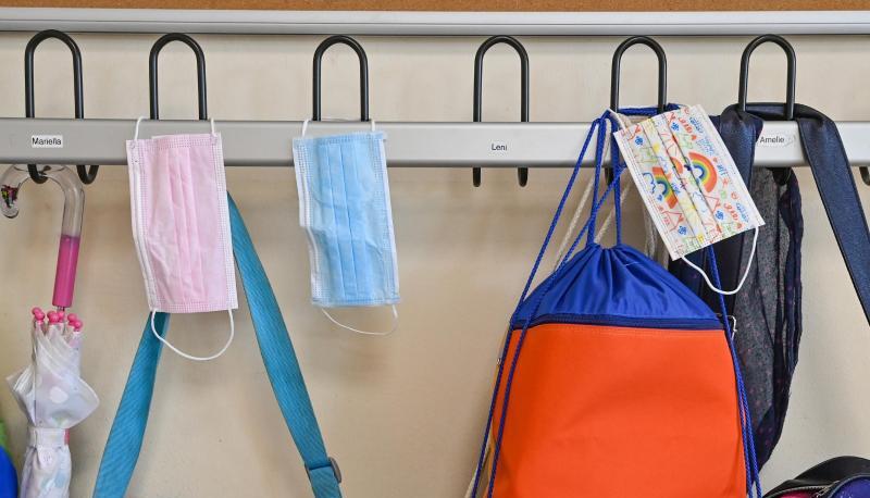 Masken und Taschen hängen in einer Grundschule an Kleiderhaken.