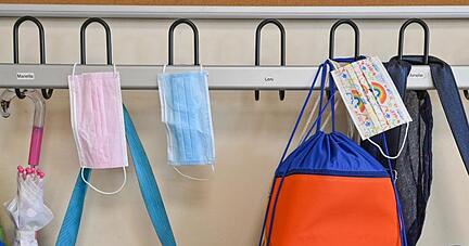Masken und Taschen hängen in einer Grundschule an Kleiderhaken. Masken und Taschen hängen in einer Grundschule an Kleiderhaken.