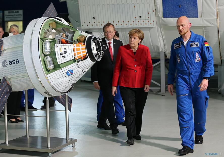 Bundeskanzlerin Angela Merkel (CDU, Mitte), der deutsche Astronaut Alexander Gerst (r) und der Generaldirektor der Europäischen Weltraumorganisation ESA, Jan Wörner, betrachten am 18.05.2016 in Köln (Nordrhein-Westfalen) beim Besuch im Europäischen Astronautenzentrum (EAC) die Raumkapsel Orion. Diese soll in Zukunft Menschen zum Mond, zu Asteroiden und vielleicht sogar zum Mars bringen. Foto: dpa