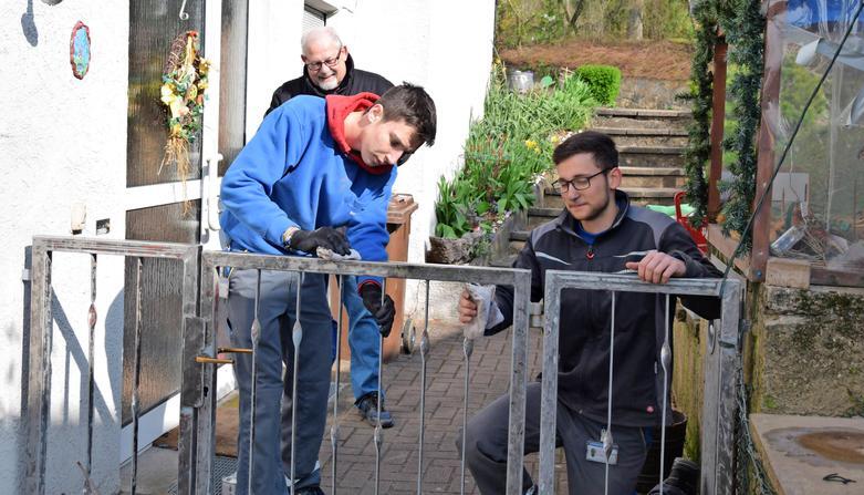 Die Dieffenbacher-Auszubildenden Lukas Dischinger (rechts) und Felix Staudt sowie Claus Hartmann aus der evangelischen Kirchengemeinde streichen die Gartentür einer älteren Dame neu.Foto: Gabriele Schneider