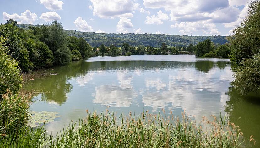 Einzelne Wolken ziehen über einen Badesee hinweg.