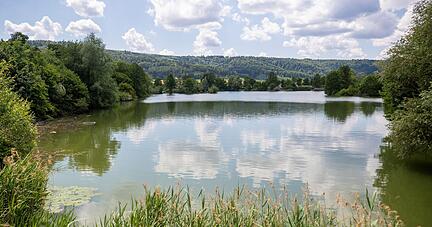 Einzelne Wolken ziehen über einen Badesee hinweg.