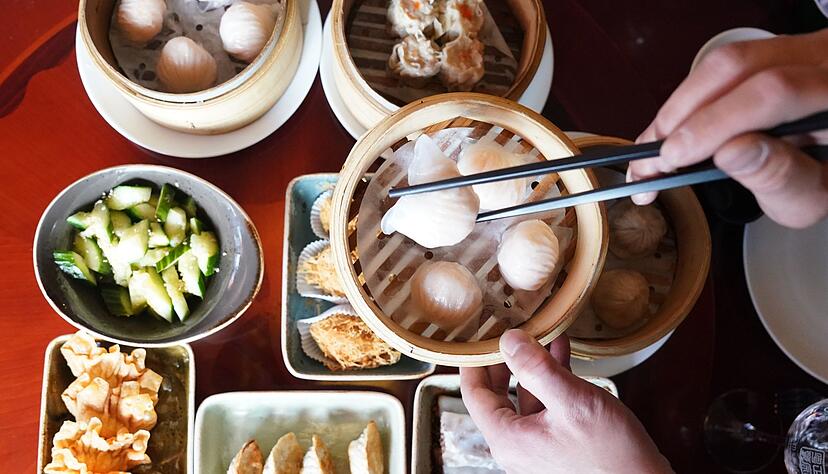 Ein Mann greift mit Essstäbchen nach Dim sum, gedämpften Teigtaschen, in einem Bambuskorb.