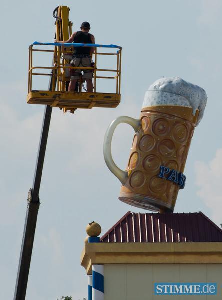 Ein Arbeiter schwebt am 29.08.2013 auf dem Oktoberfestgelände in München (Bayern) auf einer Hebebühne an einem überdimensionalem Bierkrug vorbei, der die Turmspitze eines Bierzeltes schmückt. Seit dem 15. Juli 2013 wird das größte Volksfest der Welt aufgebaut. Das Oktoberfest dauert dieses Jahr vom 21. September - 06. Oktober 2013. Foto: Peter Kneffel/dpa +++(c) dpa - Bildfunk+++