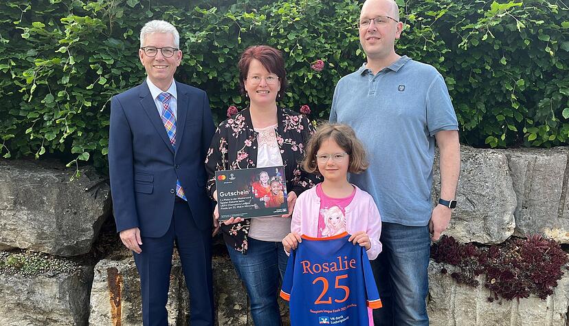Ist schon sehr gespannt auf M&uuml;nchen: das Champions-League-Einlaufkind Rosalie Gemperlein, eingerahmt von Mutter Katja und Vater Volker. VR-Bank-Filialleiter Jochen Brauchle (links) freut sich bei der Gewinn&uuml;bergabe in Hessigheim mit.
