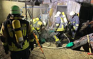 Einsatzkr&auml;fte der Feuerwehr tragen Brandreste aus dem Container.