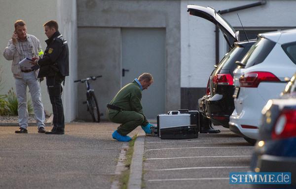Polizisten und ein Beamter der Spurensicherung halten sich in unmittelbarer Nähe zum Tatort auf einem Parkplatz auf.