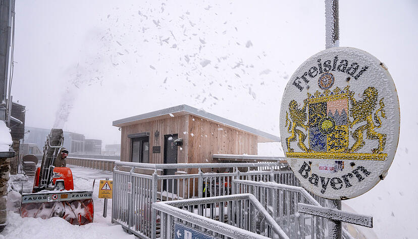 Eine Frau räumt den Neuschnee neben einem Schild mit der Aufschrift "Freistaat Bayern" auf der Aufsichtsplattform der Zugspitze. Eine Frau räumt den Neuschnee neben einem Schild mit der Aufschrift "Freistaat Bayern" auf der Aufsichtsplattform der Zugspitze.
