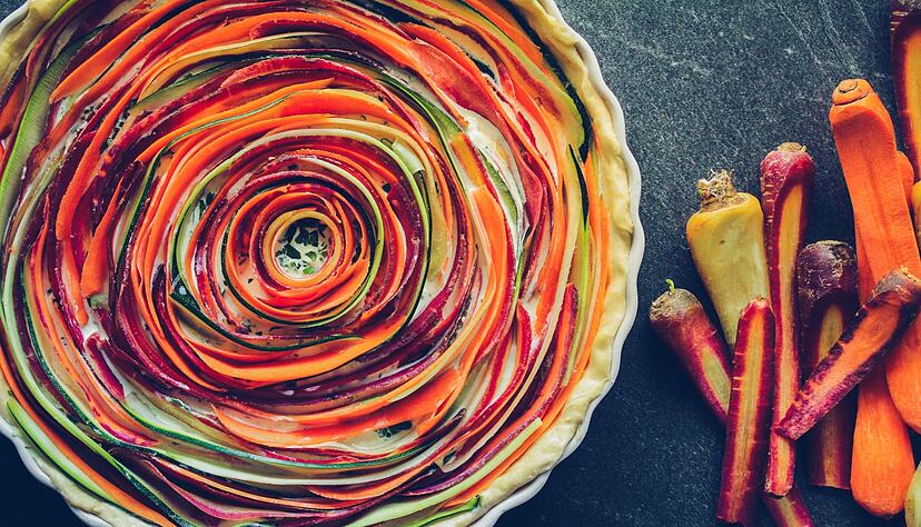 Ein echter Hingucker: Gehobelte Streifen von orangen, gelben und lila M&ouml;hren sowie einer Zucchini spiralf&ouml;rmig auf einem M&uuml;rbeteigboden mit Eier-Ziegenk&auml;segemisch legen und backen - fertig ist die Tarte.