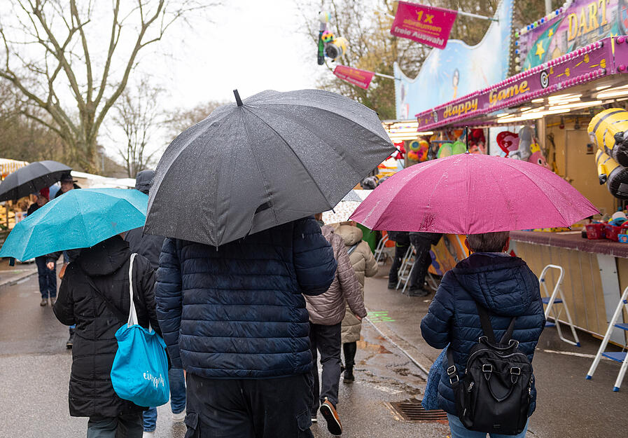 Mit Regenschirmen oder Kapuzen wagen sich einige Besucher &uuml;ber den Heilbronner Pferdemarkt am Samstag.