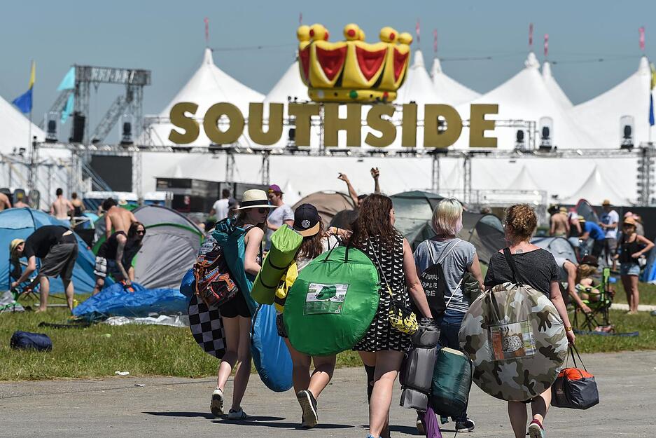 Festivalbesucher gehen &uuml;ber den Zeltplatz, w&auml;hrend im Hintergrund schon Zelte aufgebaut werden.