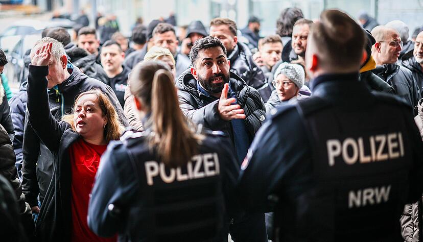 Aufgebrachte Kunden diskutieren nach dem Millionen-Raub vor der Sparkassenfiliale in Buer mit Polizeibeamten.