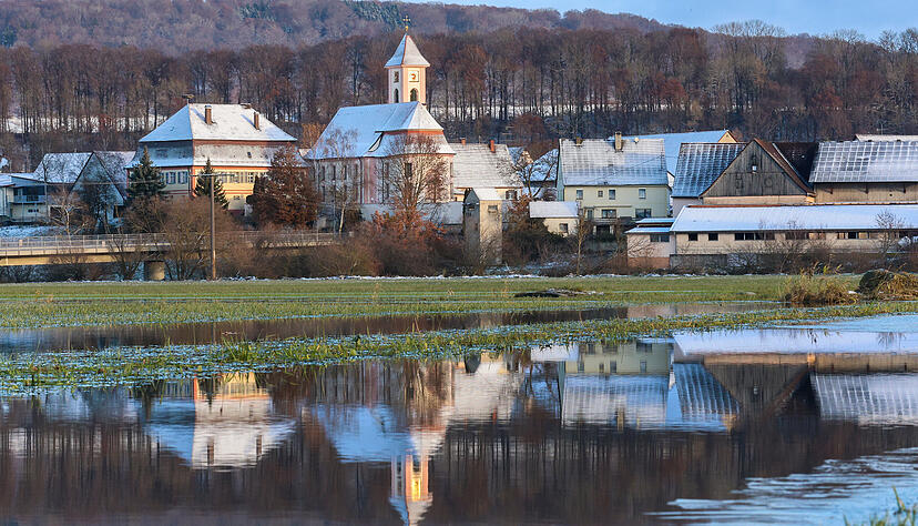 Die mit Schnee bedeckte Kirche St. Gallus in Riedlingen Zell spiegelt sich in einer überfluteten Wiese wieder.