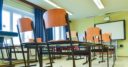 In einem leeren Unterrichtsraum an einer Schule sind die Stühle auf einen Tisch gestellt.