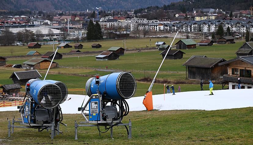 Schneekanonen stehen im Grünen neben einer Skipiste in Garmisch-Partenkirchen.