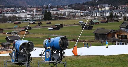 Schneekanonen stehen im Grünen neben einer Skipiste in Garmisch-Partenkirchen.