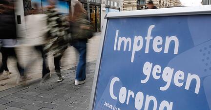 Ein Aufsteller mit dem Schriftzug „Impfen gegen Corona“ steht vor einer Apotheke.