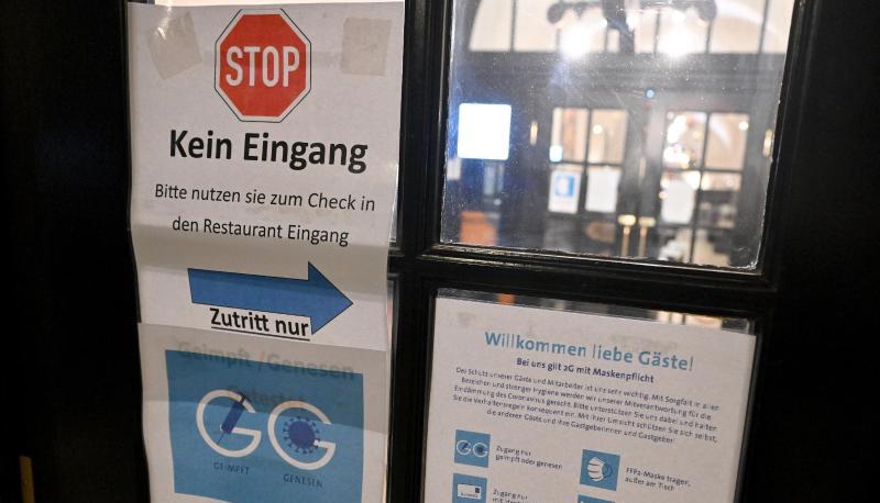 Diverse Schilder zum Einhalten der Corona-Schutzmaßnahmen hängen am Eingang zu einer Gaststätte.